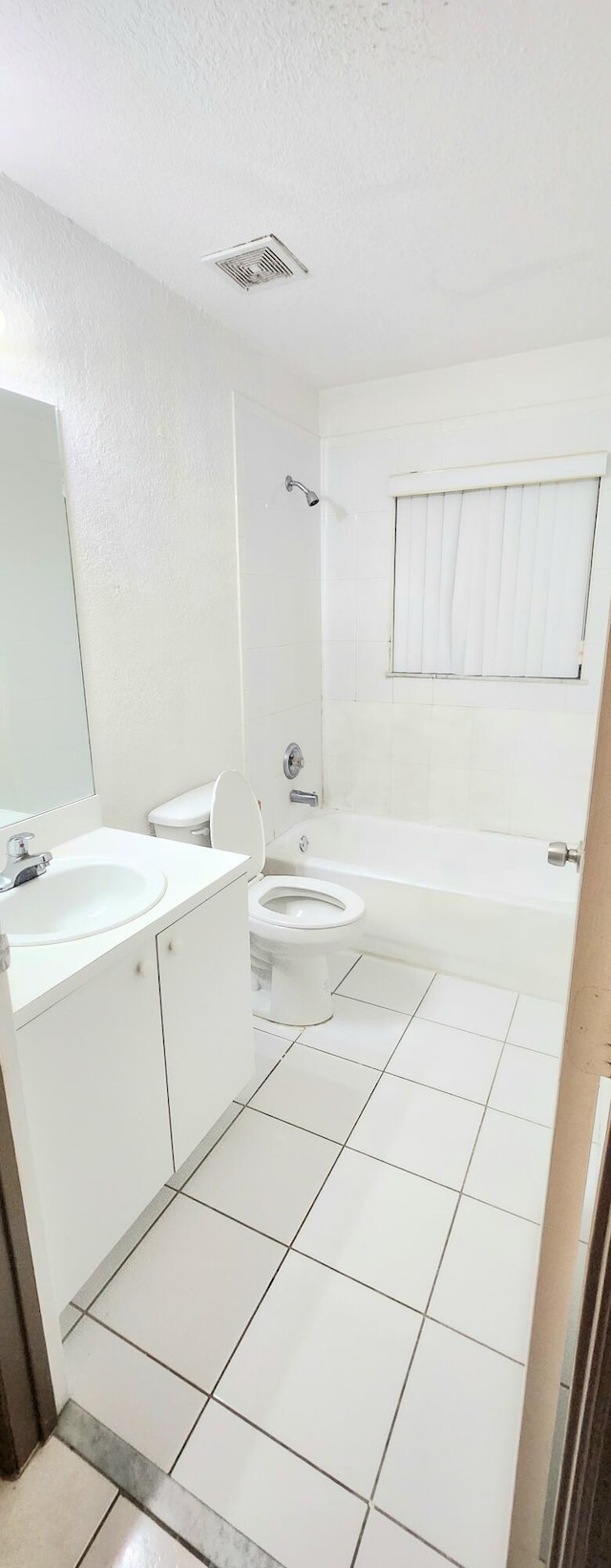 full bathroom with tile patterned floors, a textured ceiling, toilet, vanity, and tiled shower / bath