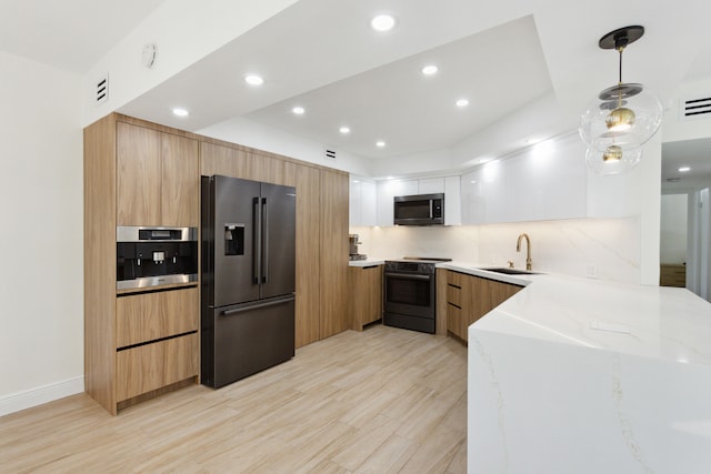 kitchen with sink, light stone counters, light hardwood / wood-style flooring, white cabinets, and appliances with stainless steel finishes