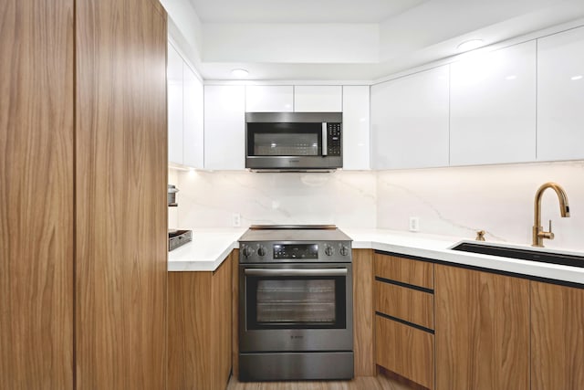 kitchen featuring backsplash, stainless steel appliances, sink, light hardwood / wood-style flooring, and white cabinetry