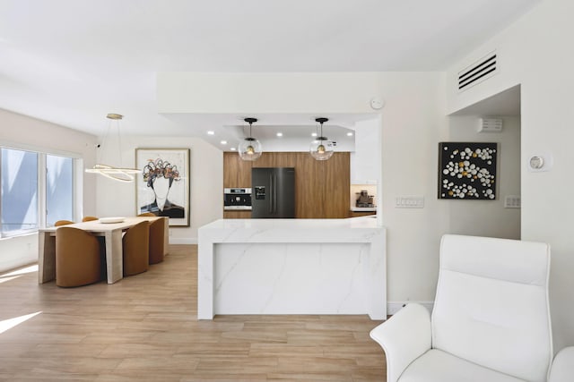 kitchen with decorative light fixtures, light wood-type flooring, a notable chandelier, black fridge with ice dispenser, and kitchen peninsula