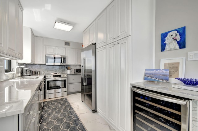 kitchen with appliances with stainless steel finishes, light stone counters, white cabinetry, sink, and wine cooler