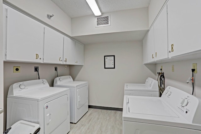 laundry area featuring a textured ceiling, light hardwood / wood-style flooring, cabinets, and washer and clothes dryer