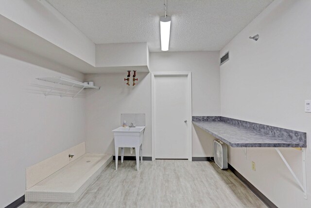 laundry area featuring light wood-type flooring and a textured ceiling