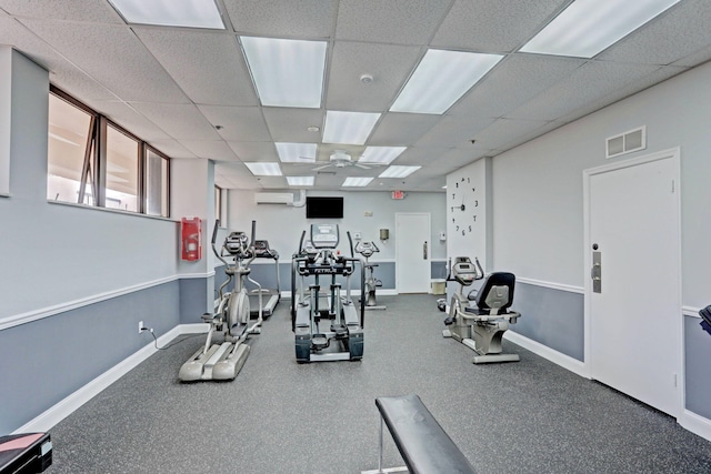 exercise room featuring a paneled ceiling, ceiling fan, and a wall mounted AC