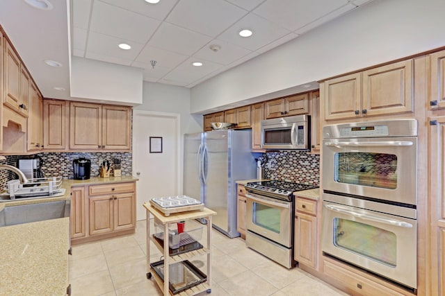 kitchen featuring backsplash, light tile patterned floors, appliances with stainless steel finishes, and light stone countertops