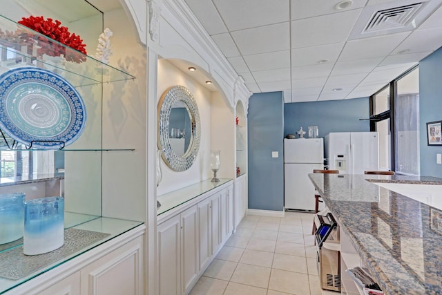 kitchen with white refrigerator with ice dispenser, white fridge, white cabinetry, light tile patterned floors, and stone countertops