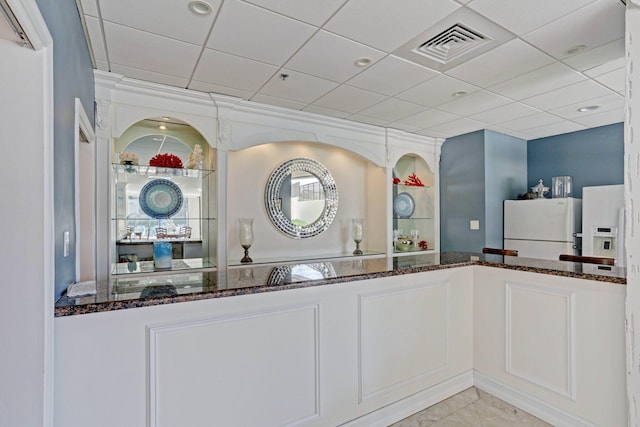 interior space with a paneled ceiling, white fridge, white refrigerator with ice dispenser, and dark stone counters