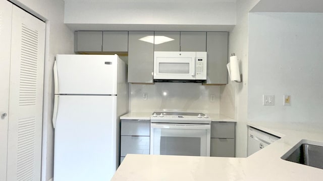 kitchen with backsplash, gray cabinetry, and white appliances