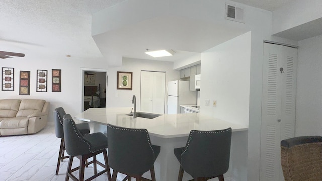 kitchen featuring a breakfast bar area, white appliances, kitchen peninsula, sink, and ceiling fan