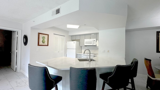 kitchen featuring white appliances, kitchen peninsula, a breakfast bar area, and gray cabinetry