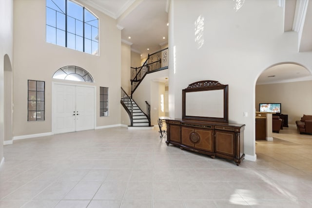 entryway featuring a towering ceiling, light tile patterned floors, and ornamental molding