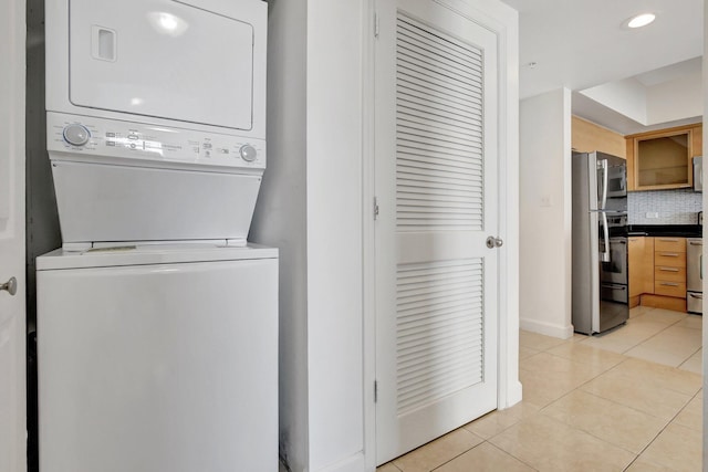 clothes washing area featuring light tile patterned flooring and stacked washing maching and dryer