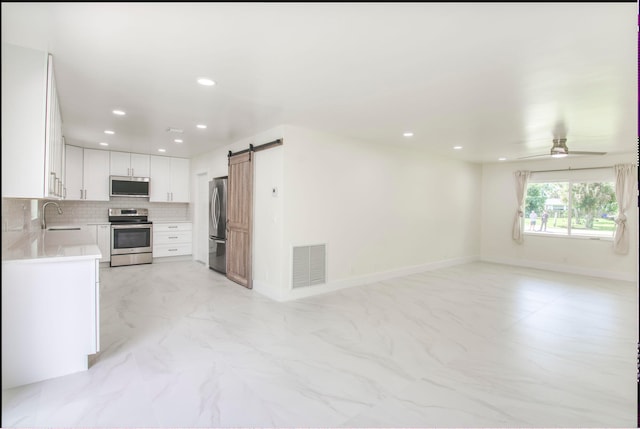 kitchen with ceiling fan, white cabinets, sink, stainless steel appliances, and a barn door