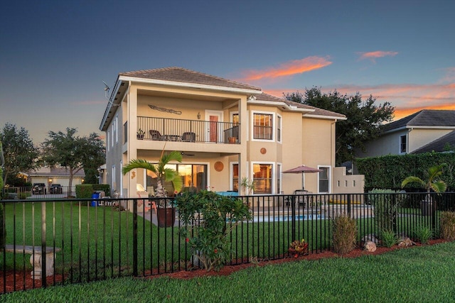 back house at dusk featuring a balcony, a swimming pool, and a yard