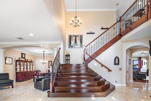 stairs with a towering ceiling, ornamental molding, a chandelier, and ornate columns