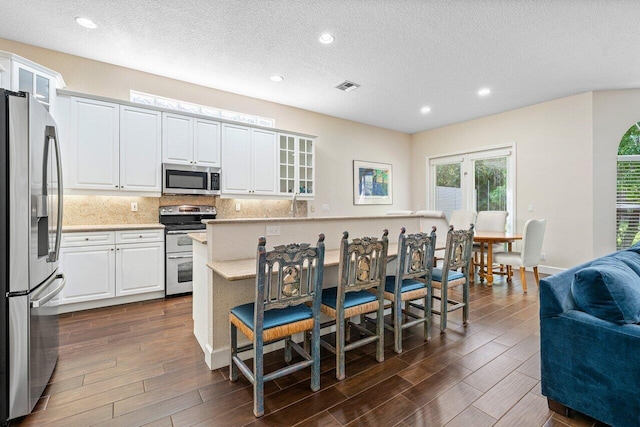 kitchen with a breakfast bar, stainless steel appliances, white cabinetry, and dark wood-type flooring