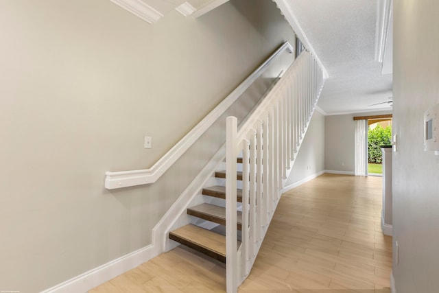 stairs with a textured ceiling, crown molding, and hardwood / wood-style flooring