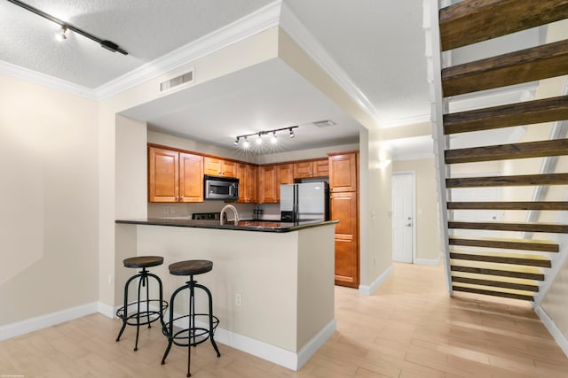 kitchen featuring a textured ceiling, track lighting, kitchen peninsula, appliances with stainless steel finishes, and crown molding