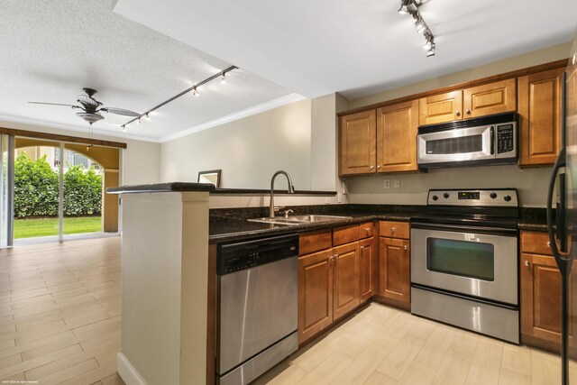 kitchen with sink, rail lighting, stainless steel appliances, dark stone countertops, and ceiling fan