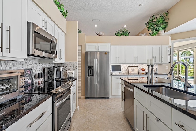 kitchen with white cabinets, appliances with stainless steel finishes, sink, and dark stone counters