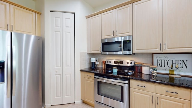 kitchen featuring light brown cabinets, appliances with stainless steel finishes, dark stone countertops, and decorative backsplash