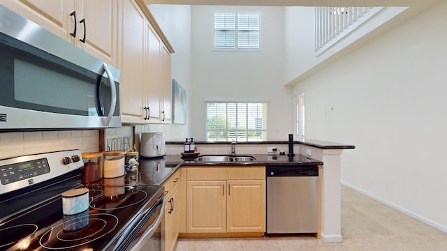 kitchen with a high ceiling, stainless steel appliances, light brown cabinetry, kitchen peninsula, and sink