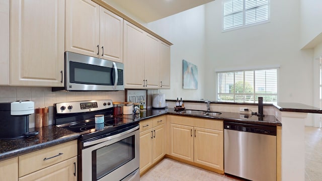 kitchen featuring dark stone countertops, kitchen peninsula, sink, decorative backsplash, and appliances with stainless steel finishes