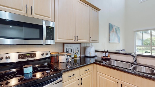 kitchen with dark stone countertops, tasteful backsplash, stainless steel appliances, light brown cabinetry, and sink