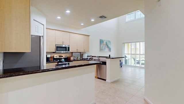 kitchen with appliances with stainless steel finishes, dark stone counters, kitchen peninsula, light tile patterned flooring, and a breakfast bar area