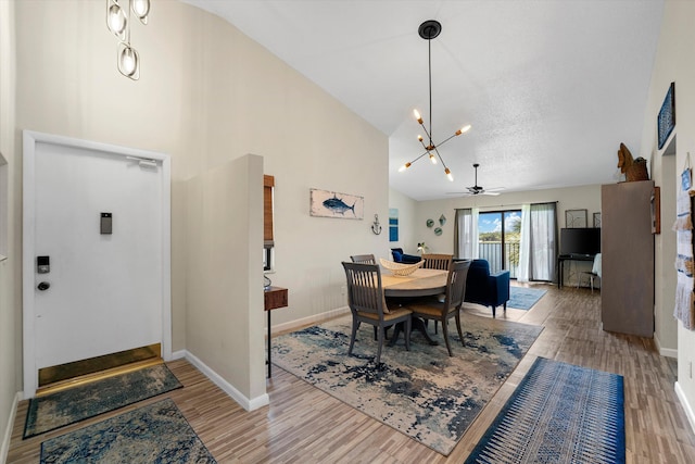 dining room with ceiling fan with notable chandelier, wood-type flooring, and high vaulted ceiling