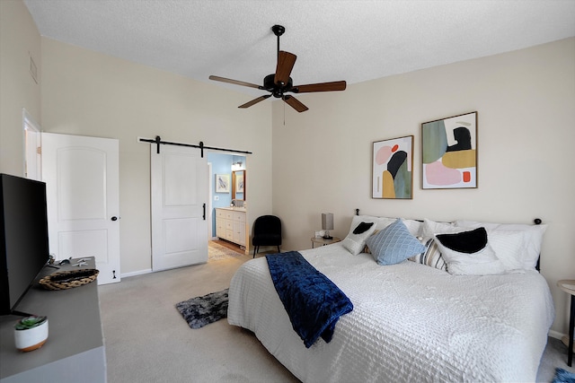 bedroom with ceiling fan, connected bathroom, a textured ceiling, light colored carpet, and a barn door