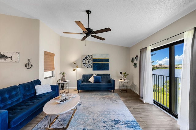 living room with a water view, a textured ceiling, wood-type flooring, lofted ceiling, and ceiling fan