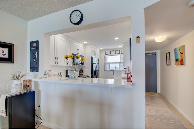 kitchen with white cabinets, stainless steel refrigerator, kitchen peninsula, and a textured ceiling