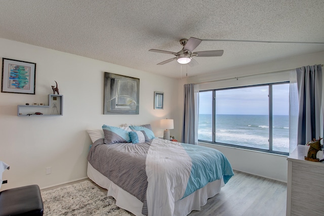 bedroom with ceiling fan, a textured ceiling, light hardwood / wood-style floors, and a water view