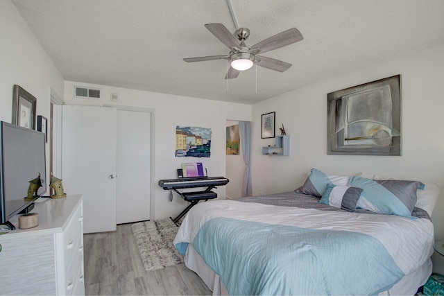 bedroom featuring a textured ceiling, light wood-type flooring, ceiling fan, and a closet