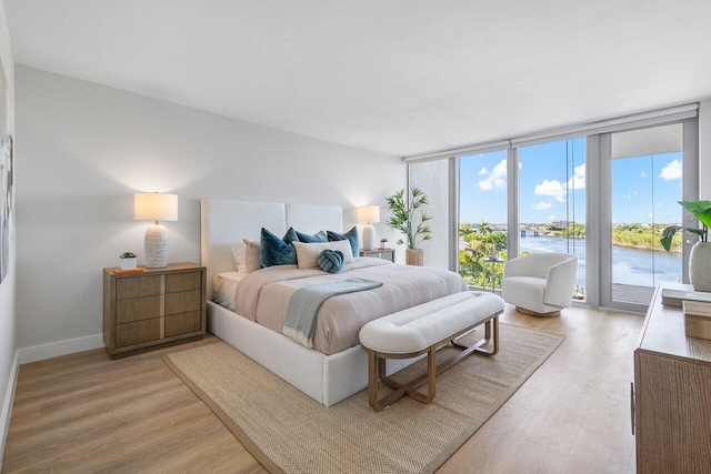 bedroom with access to exterior, floor to ceiling windows, a water view, and light hardwood / wood-style floors