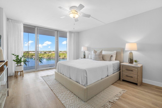 bedroom featuring light hardwood / wood-style flooring, ceiling fan, a water view, and access to outside