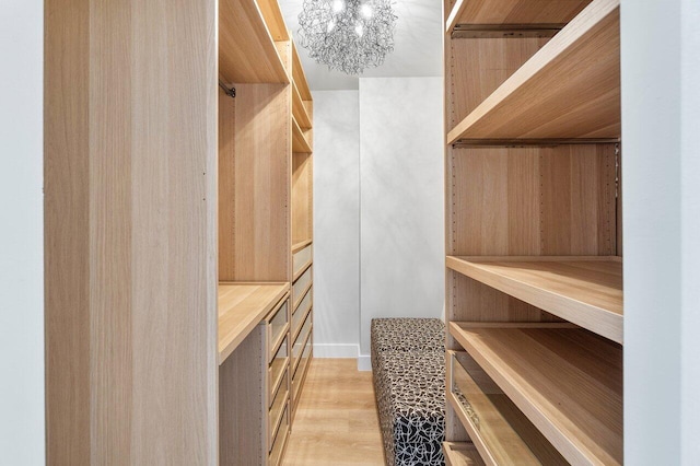 spacious closet with light wood-type flooring and an inviting chandelier