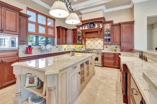 kitchen with an island with sink, hanging light fixtures, sink, backsplash, and appliances with stainless steel finishes