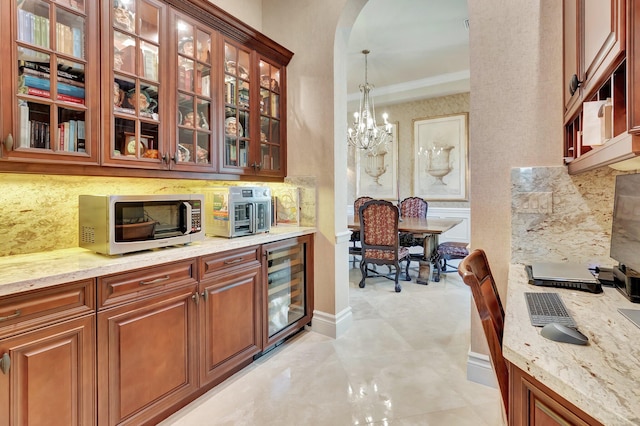 kitchen featuring a notable chandelier, beverage cooler, light stone counters, and pendant lighting