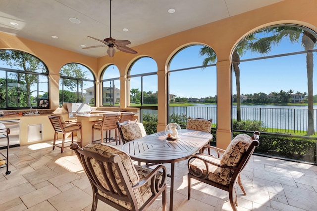 sunroom with ceiling fan and a water view