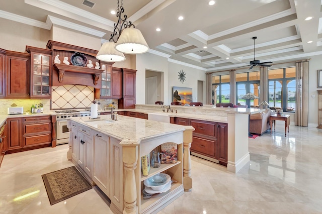 kitchen with high end white range, ornamental molding, ceiling fan, and an island with sink