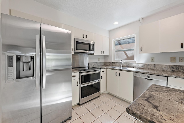 kitchen with a textured ceiling, appliances with stainless steel finishes, sink, white cabinets, and light tile patterned flooring