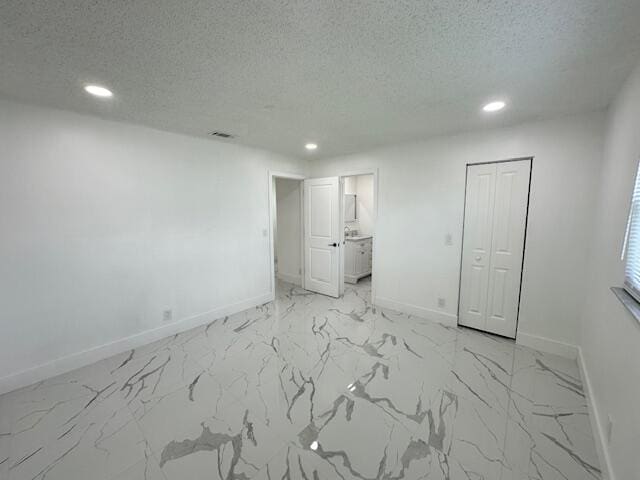 unfurnished bedroom with a textured ceiling, ensuite bathroom, and a closet