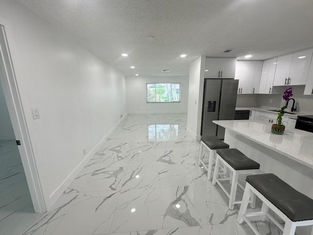 kitchen with white cabinets, sink, a kitchen bar, stainless steel fridge with ice dispenser, and a textured ceiling