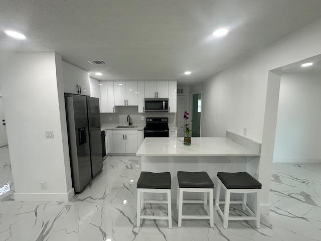 kitchen with a textured ceiling, a breakfast bar, stainless steel appliances, kitchen peninsula, and white cabinetry