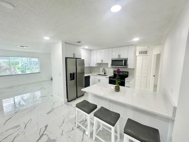 kitchen with a kitchen bar, kitchen peninsula, sink, appliances with stainless steel finishes, and white cabinets