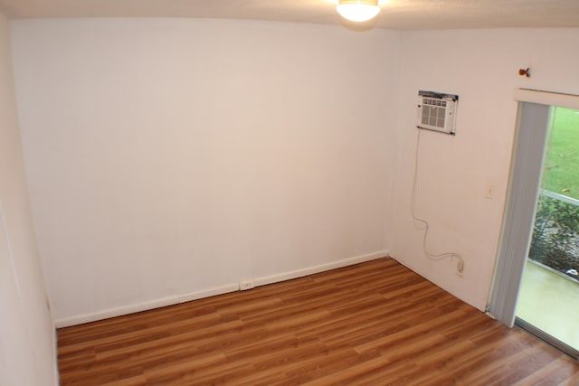 unfurnished room with a wall mounted AC, vaulted ceiling, and hardwood / wood-style floors