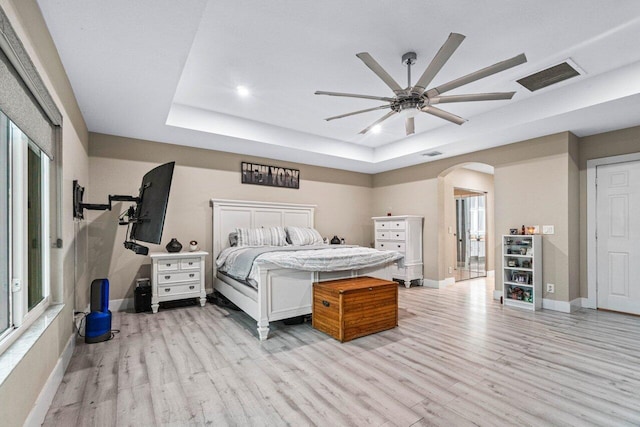 bedroom with arched walkways, baseboards, light wood-type flooring, a tray ceiling, and visible vents