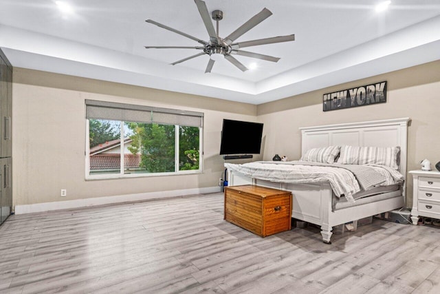 bedroom featuring baseboards, ceiling fan, wood finished floors, and a raised ceiling